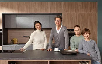 Glückliche Familie, die vor einer modernen Küche mit Holz und grauen Elementen steht.