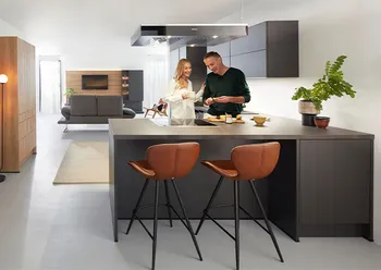 Zwei Personen in einer modernen schwarzen Küche mit Holzhochschränken.